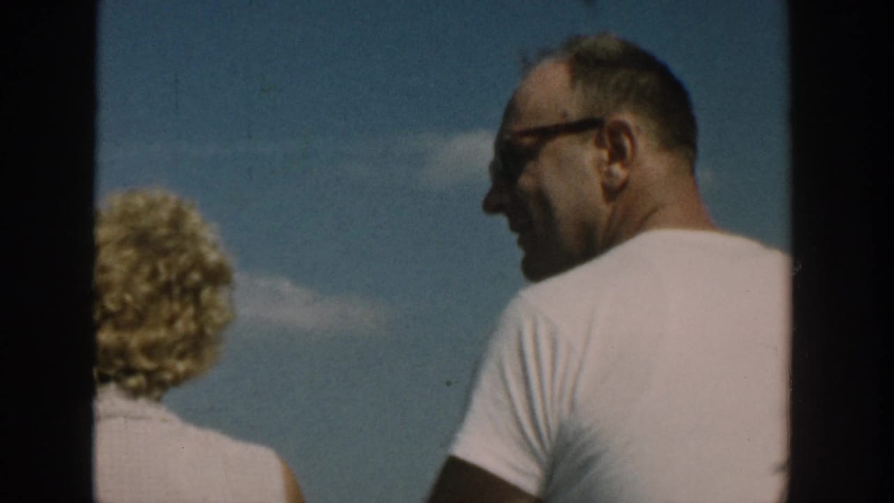 Man in sunglasses and white shirt beside a blonde woman under a blue sky.