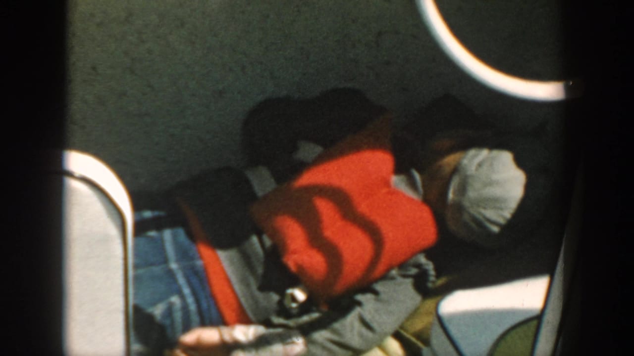 Passenger reclines in a boat wearing a red life jacket and light cap.