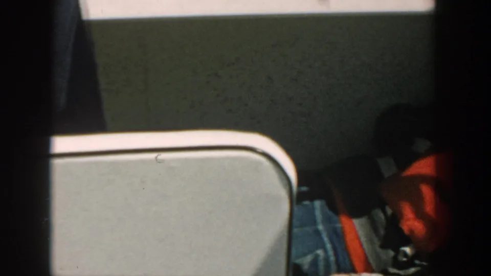 Close boat detail shows a red life jacket, denim clothing, light upholstery, and a rounded metal rail in the 8mm frame.