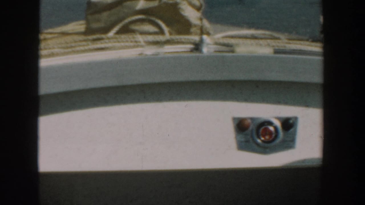 Close view of a white boat console with controls and a person's denim-clad legs at the edge of frame.