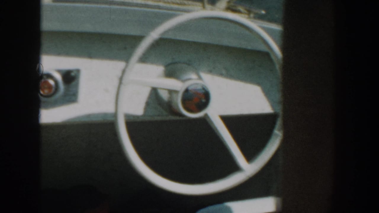 1957 Wisconsin home-movie frame of a white boat steering wheel, simple dashboard controls, and sunlit console surfaces.