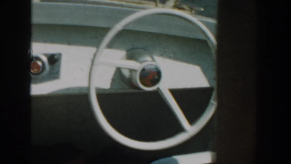 1957 Wisconsin home-movie frame of a white boat steering wheel, simple dashboard controls, and sunlit console surfaces.