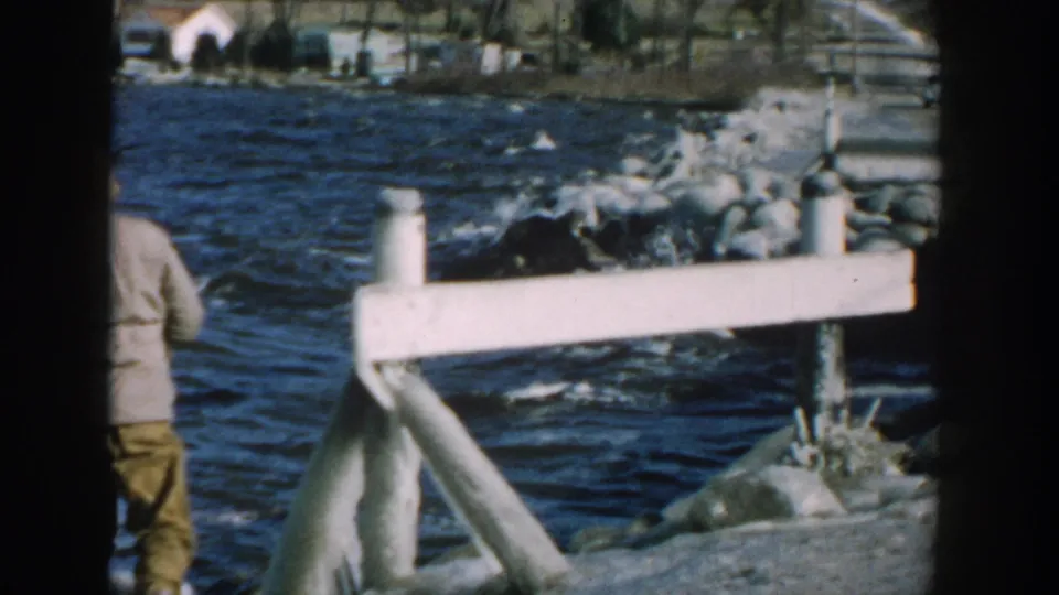 The frame emphasizes the small dock or shoreline structure, rocks, and choppy lake, with the adult partly cropped at left.