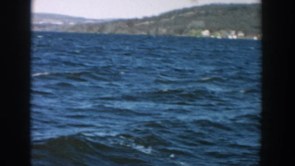 1957 Wisconsin home-movie view across choppy lake water toward low hills and small shoreline structures.