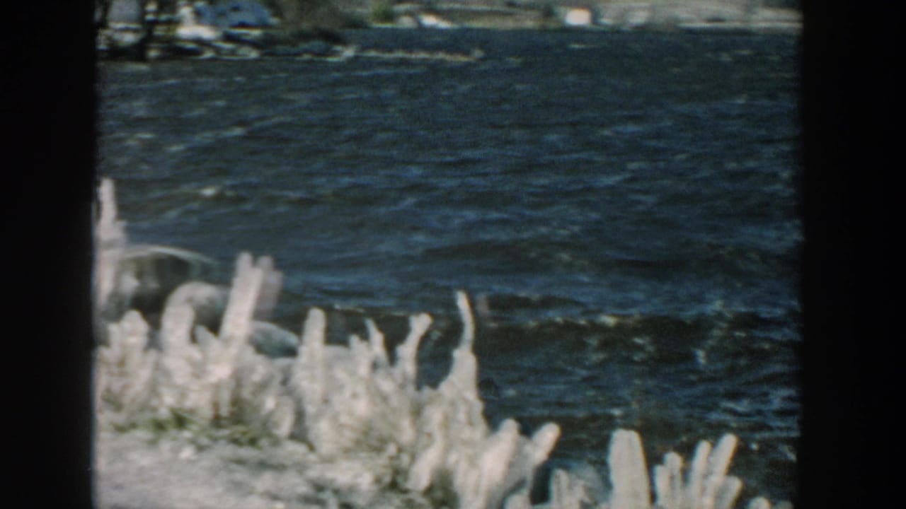 Rippling lake water beside pale shoreline ice or rocks, framed by dark film borders.