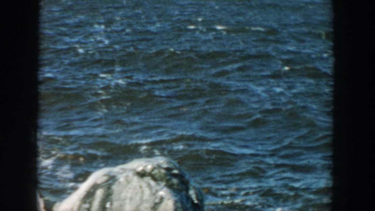 1957 Wisconsin 8mm view of textured lake water with a pale shoreline rock or icy form near the foreground.