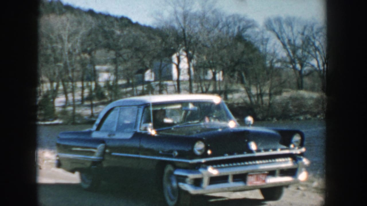 Wisconsin 1957 frame of a dark blue chrome-trim sedan with white roof and whitewall tires beside a river.