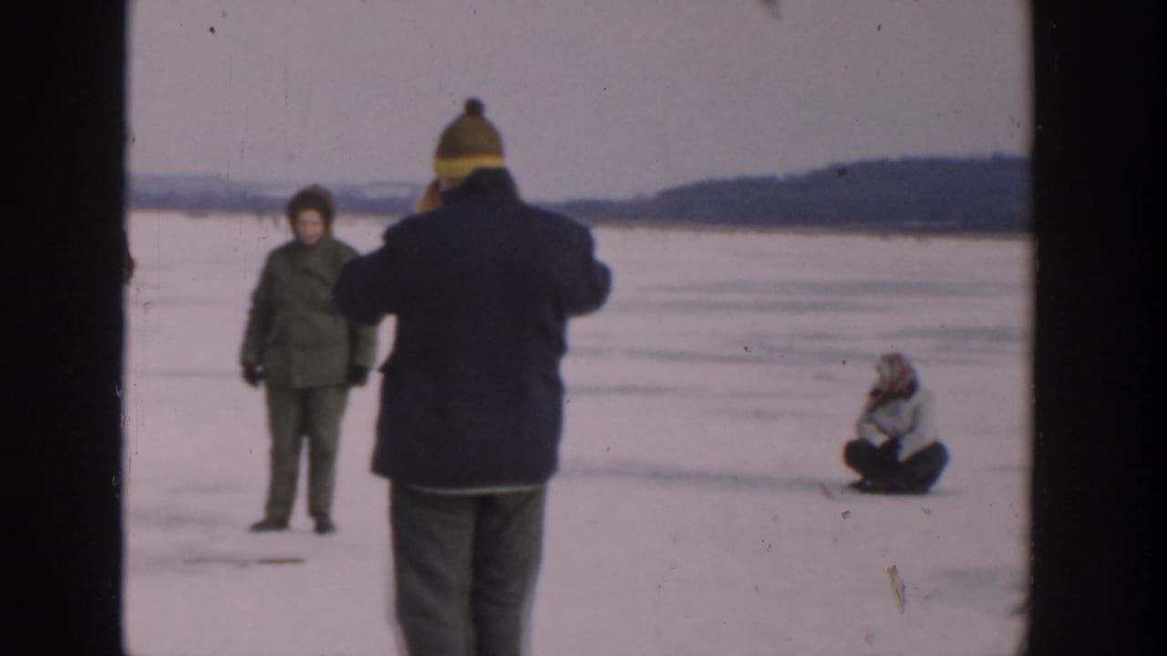 Bundled people on a frozen lake, with one person facing away toward others on the ice.