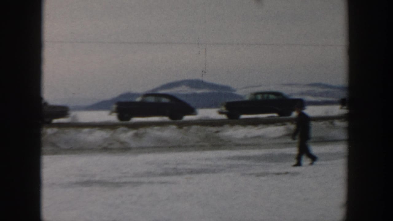 Person walking across snow with classic cars on the road behind.