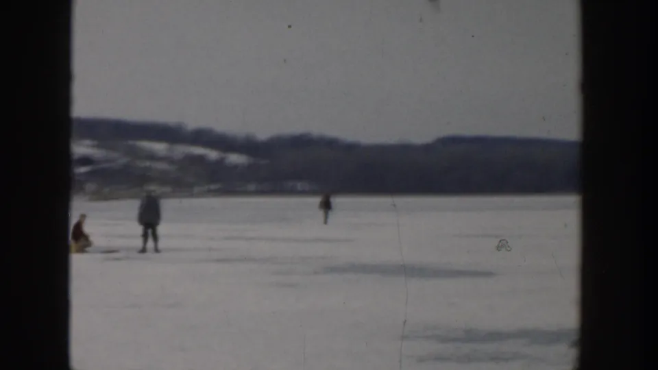 Wide 1957 Wisconsin home-movie view of people ice fishing across a frozen lake under an overcast sky.