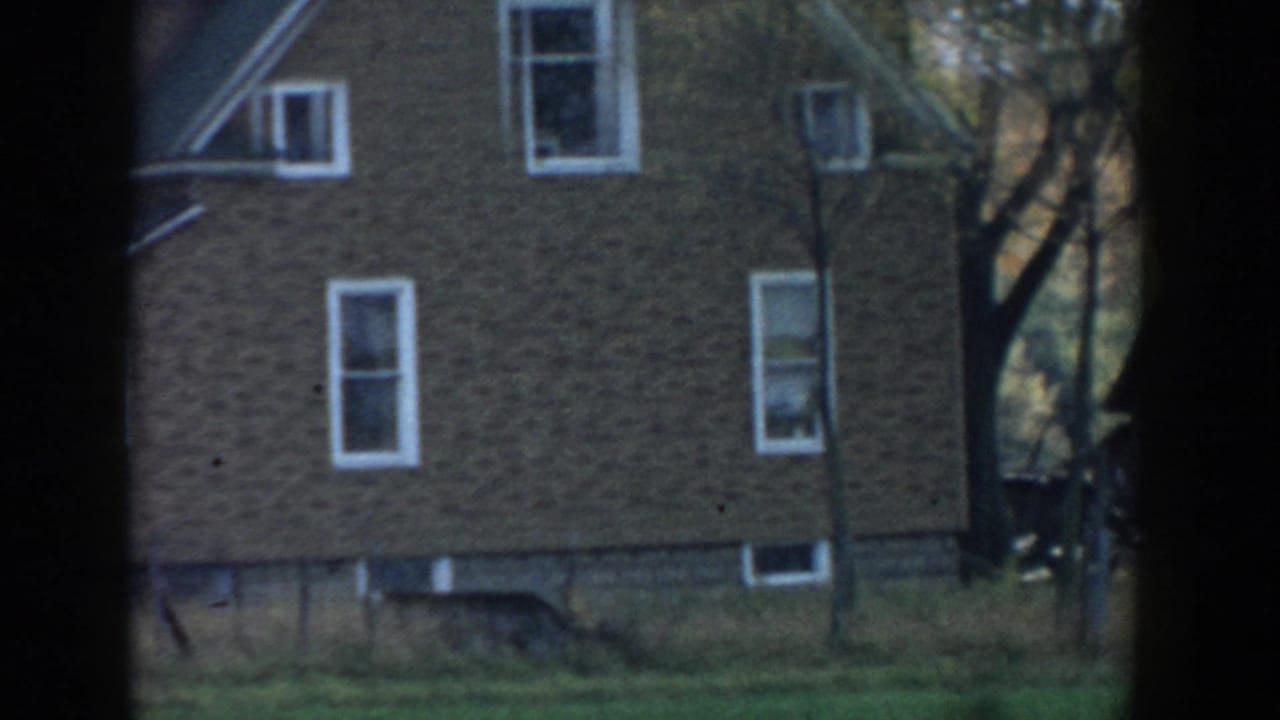 1958 Michigan 8mm frame showing part of a brown brick house with white-trimmed windows, grass, and dark vignette edges.