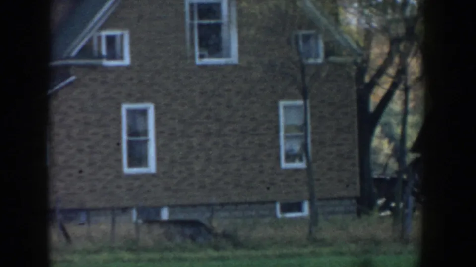 1958 Michigan 8mm frame showing part of a brown brick house with white-trimmed windows, grass, and dark vignette edges.