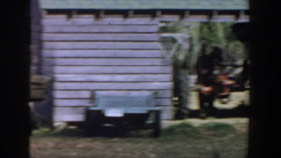 A 1958 Michigan backyard frame shows an outbuilding, a light trailer or bin, and yard equipment with the dog partly obscured at right.
