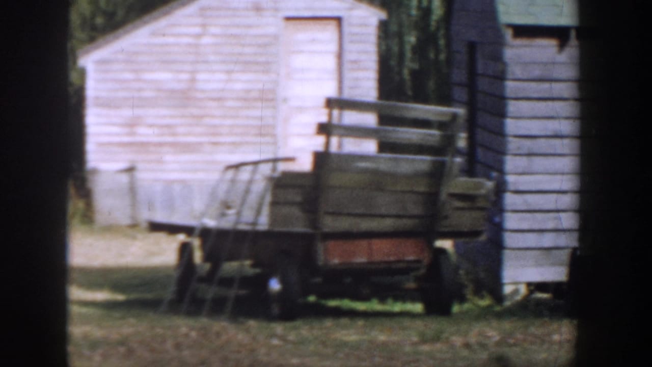 1958 Michigan 8mm frame showing a wooden cart beside a white shed, with grass and trees in the background.
