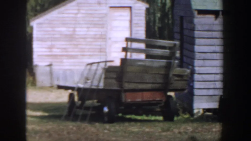 1958 Michigan 8mm frame showing a wooden cart beside a white shed, with grass and trees in the background.