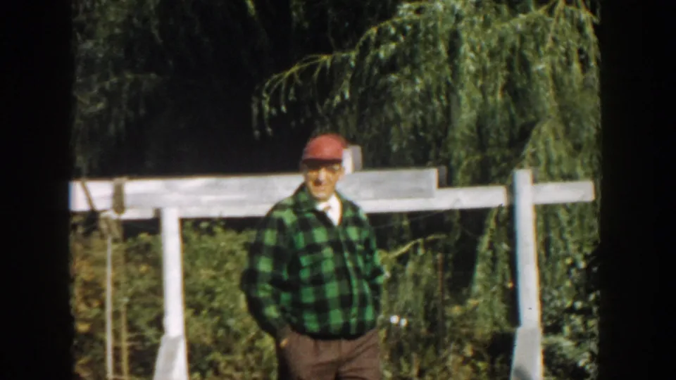 The 1958 Michigan frame shows the man walking through the garden area, with a white fence and drooping tree branches behind him.