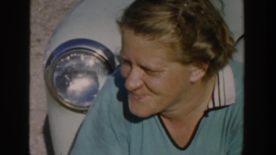 In the final frame, the woman turns sideways and smiles near the car headlight in a rural Michigan 1958 home-movie scene.