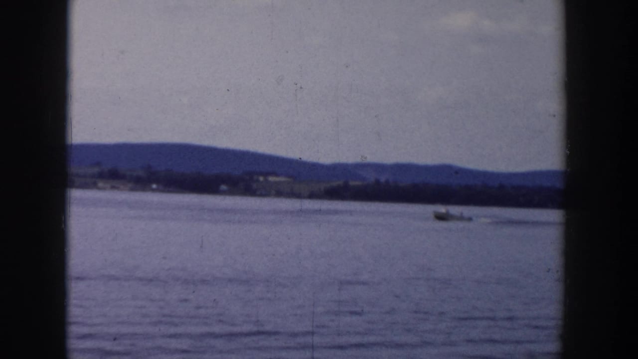 Wide lake view with a small boat and distant hills under a cloudy sky.
