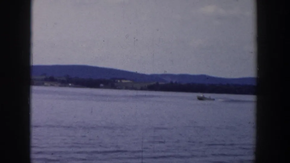 Wide 1958 Wisconsin lake view with a small boat on the water and low hills in the distance.