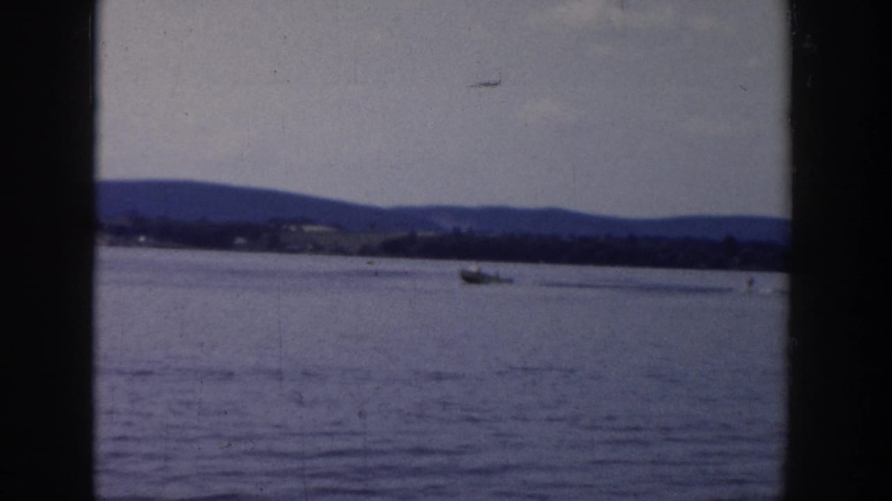 Distant boat on a Wisconsin lake in 1958, filmed in soft 8mm color with hills across the horizon.