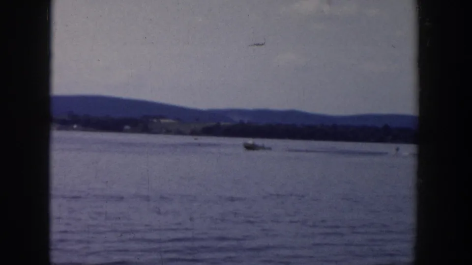 Distant boat on a Wisconsin lake in 1958, filmed in soft 8mm color with hills across the horizon.