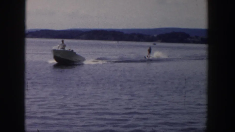 1958 Wisconsin waterskiing frame with a motorboat pulling a skier across calm lake water.
