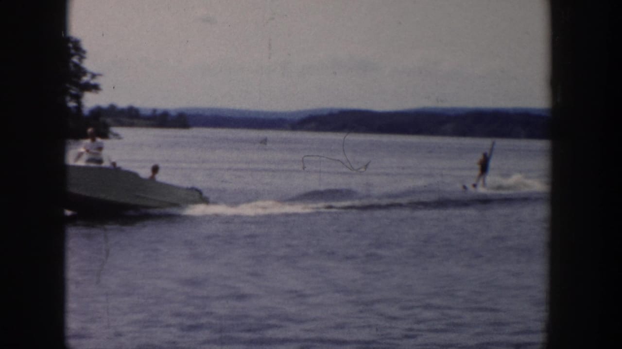 Motorboat and water skier move across open lake water with shoreline in the distance.