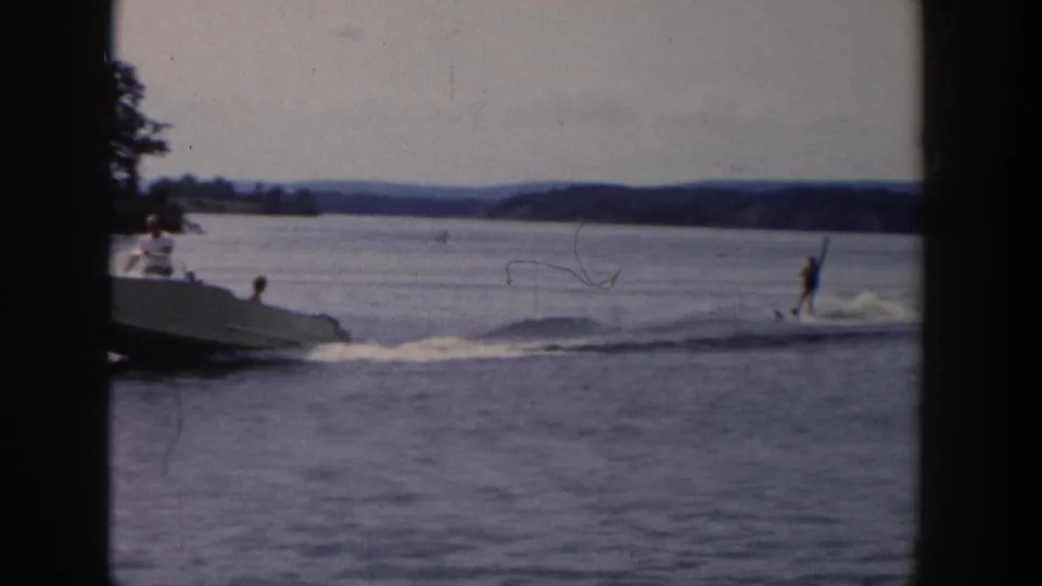 The boat continues towing the skier across a Wisconsin lake, with spray trailing behind and dark 8mm frame borders visible.