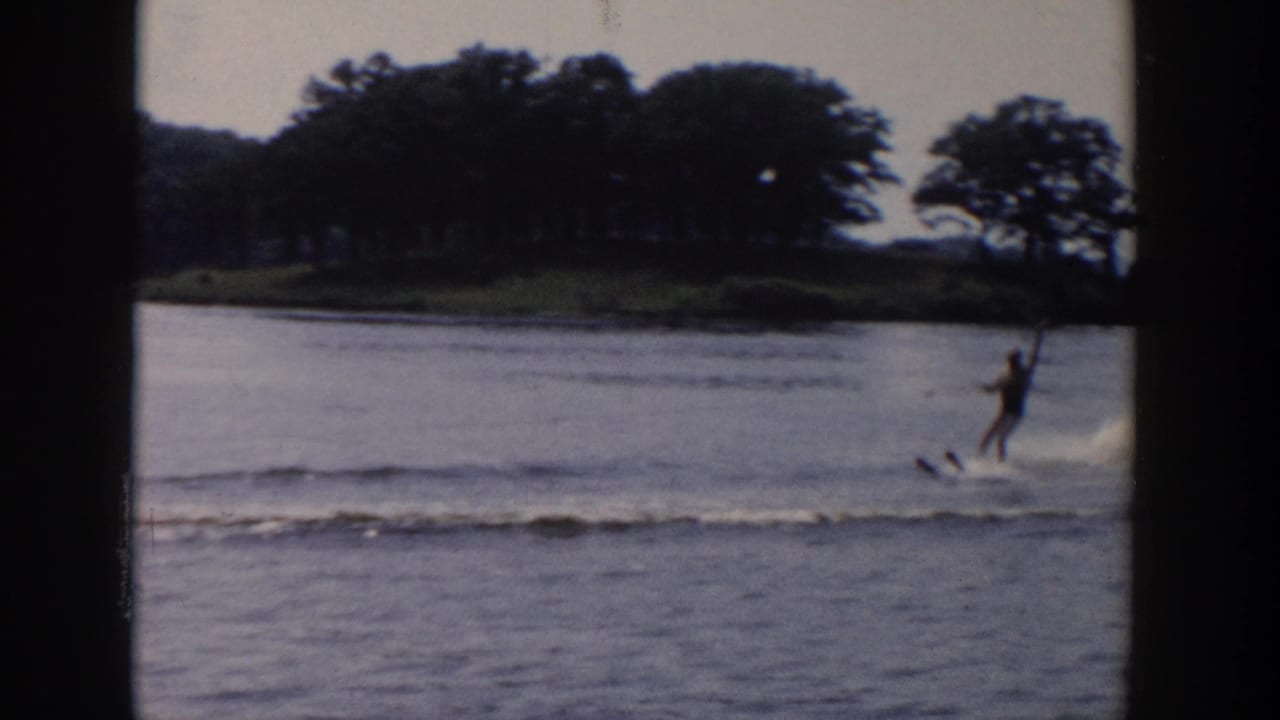 Man water skiing across a lake with a wooded shoreline behind him.
