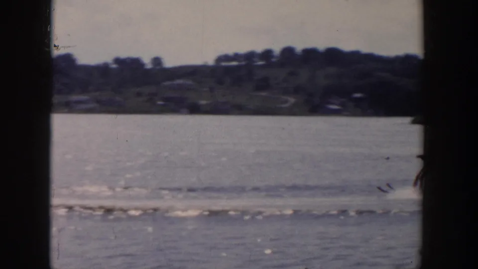 Wisconsin lake view from 1958 footage, with a skier partly near the frame edge and wake lines across the water.