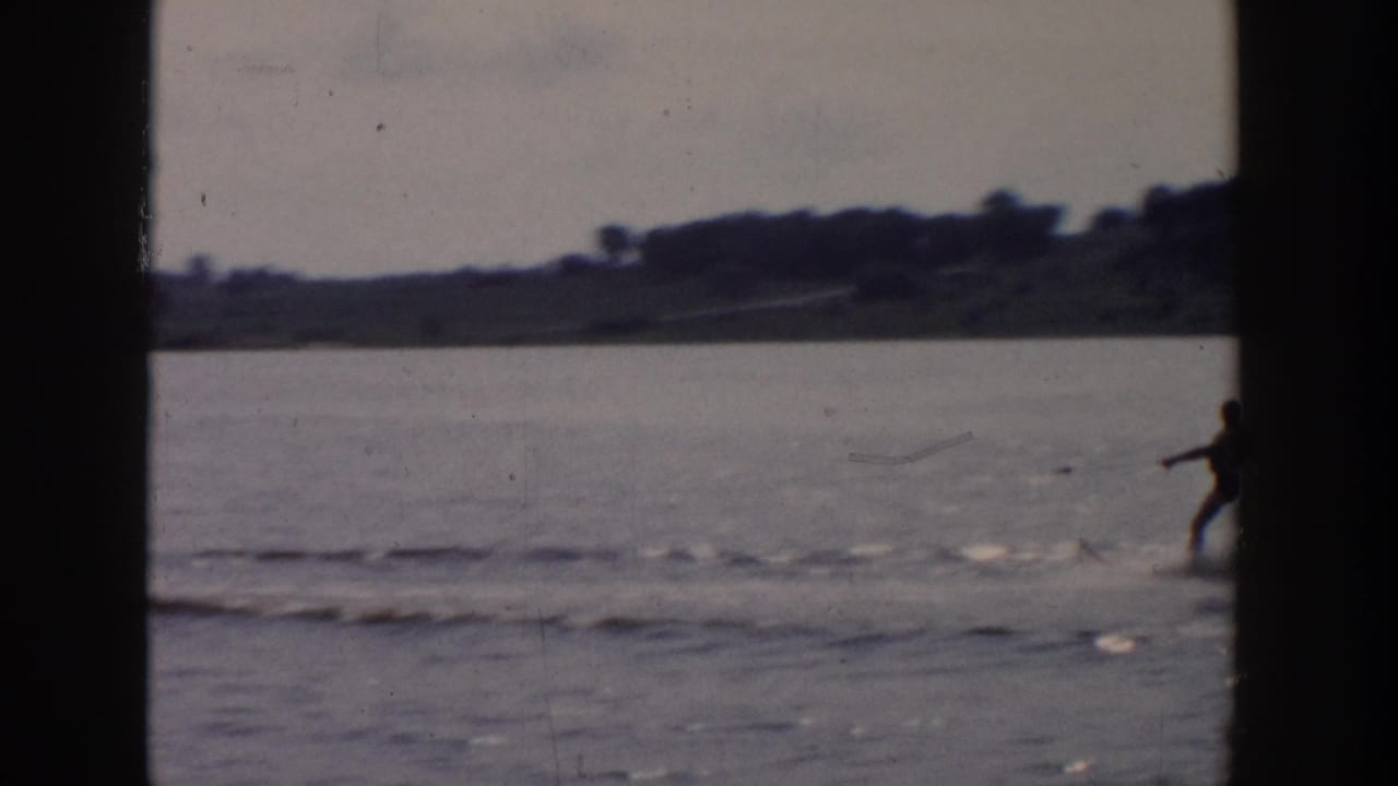 Distant water skier on a Wisconsin lake in 1958 home-movie footage, with low shoreline and soft film grain visible.