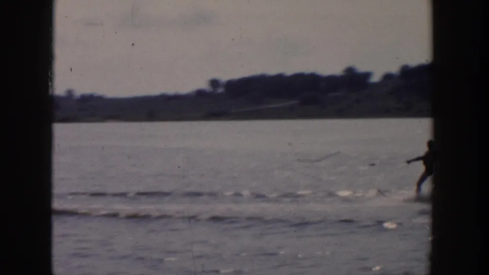 Distant water skier on a Wisconsin lake in 1958 home-movie footage, with low shoreline and soft film grain visible.