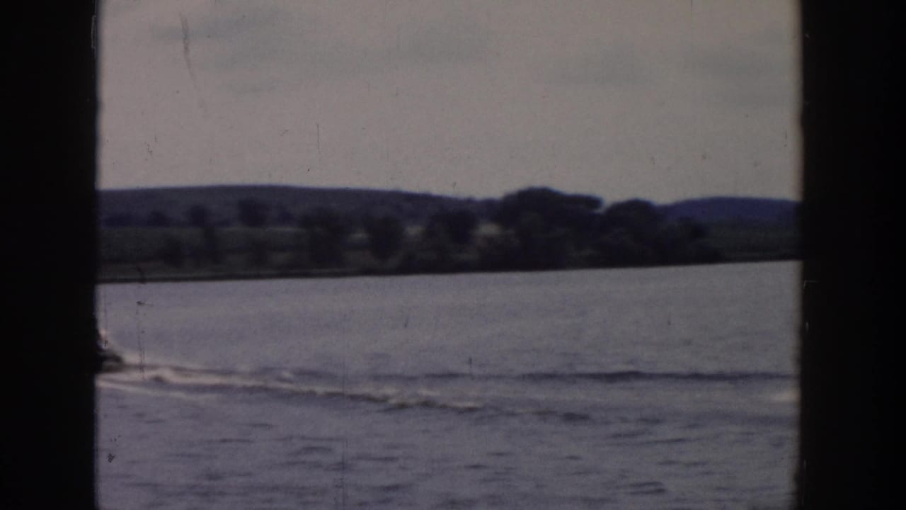 End frame of the 1958 Wisconsin lake scene, showing the skier near the edge, wake marks, and wooded shoreline beyond.