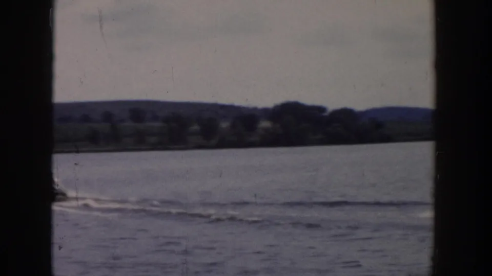 End frame of the 1958 Wisconsin lake scene, showing the skier near the edge, wake marks, and wooded shoreline beyond.