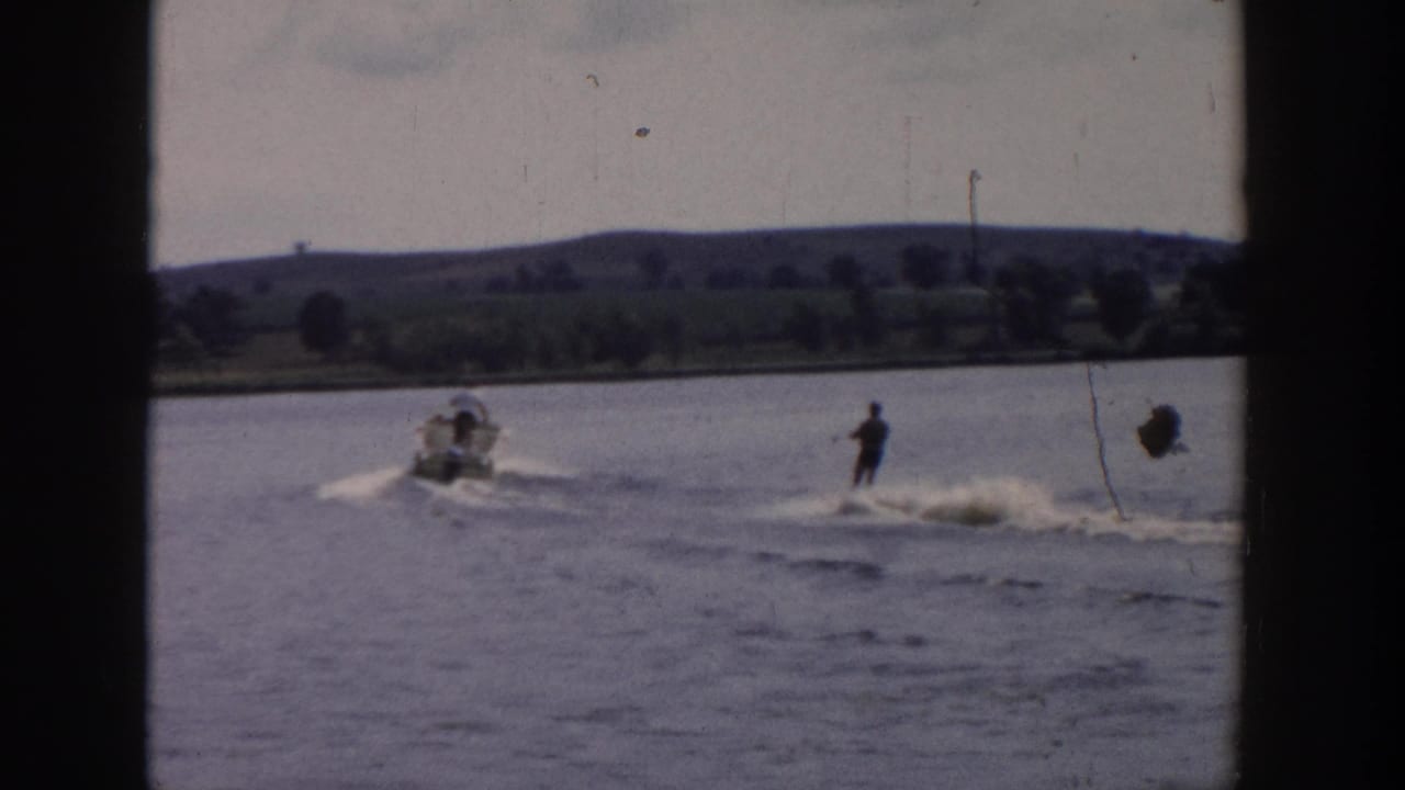 1958 Wisconsin home-movie frame showing a water skier being pulled behind a small motorboat on a rural lake.