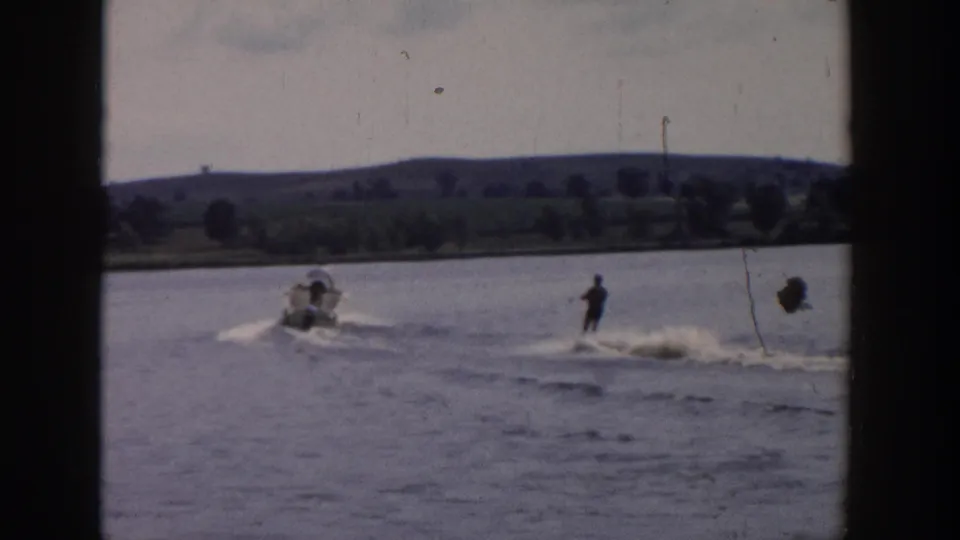 1958 Wisconsin home-movie frame showing a water skier being pulled behind a small motorboat on a rural lake.