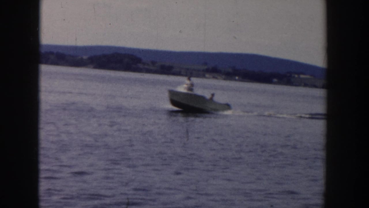 1958 Wisconsin 8mm frame showing a small motorboat on calm lake water with a water skier following in its wake.