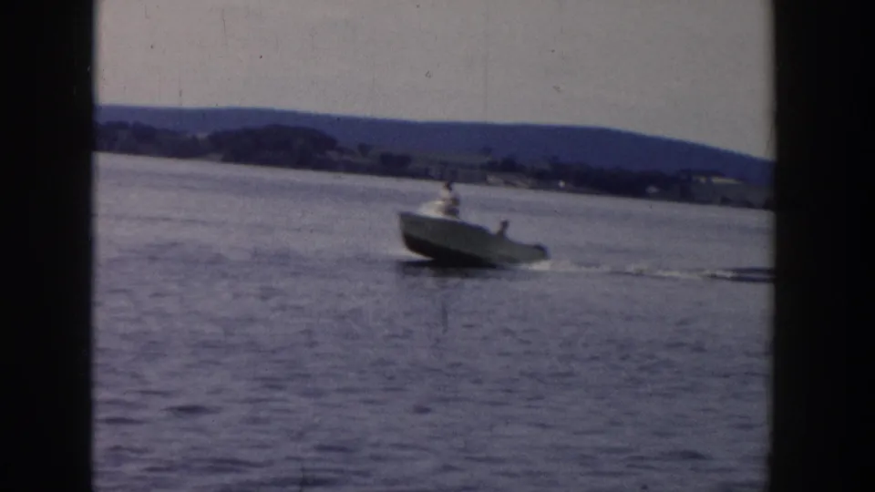 1958 Wisconsin 8mm frame showing a small motorboat on calm lake water with a water skier following in its wake.