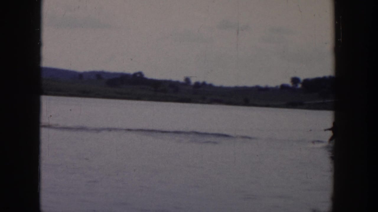 The skier is partly at the edge of the 8mm frame while a long wake cuts across the lake toward the distant shore.