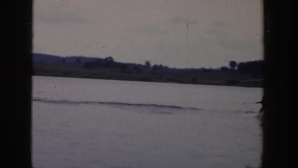 The skier is partly at the edge of the 8mm frame while a long wake cuts across the lake toward the distant shore.