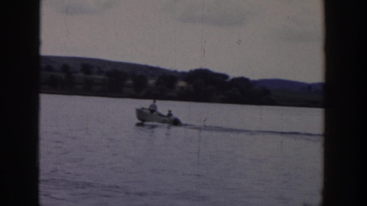A small motorboat carrying visible occupants moves across the Wisconsin lake, towing the water skier outside the frame.