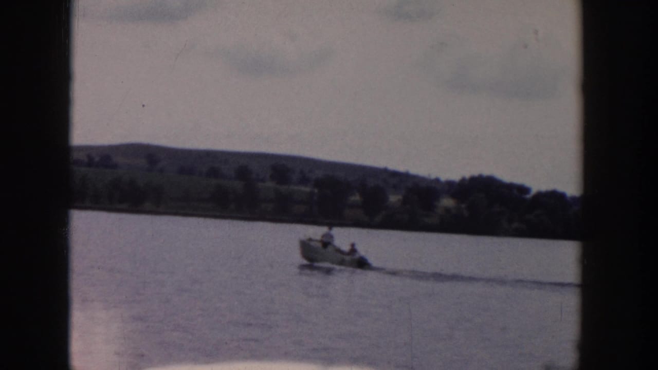 Small motorboat towing a distant water skier across calm water with hills beyond.