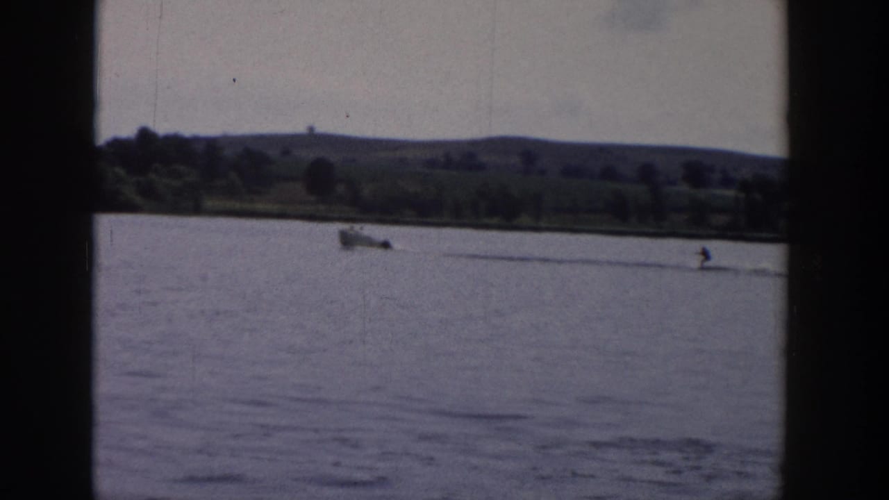 The final 1958 Wisconsin frame shows the small boat and distant water skier nearing the right side of the lagoon view, with shoreline greenery behind.