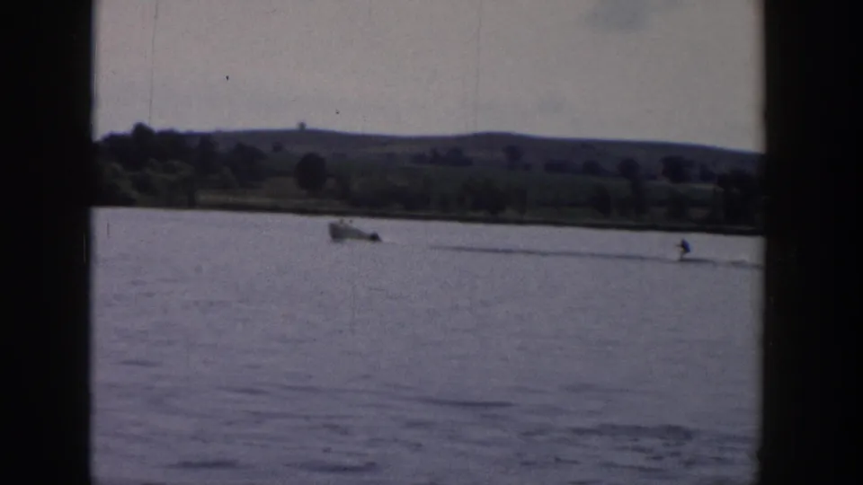 The final 1958 Wisconsin frame shows the small boat and distant water skier nearing the right side of the lagoon view, with shoreline greenery behind.
