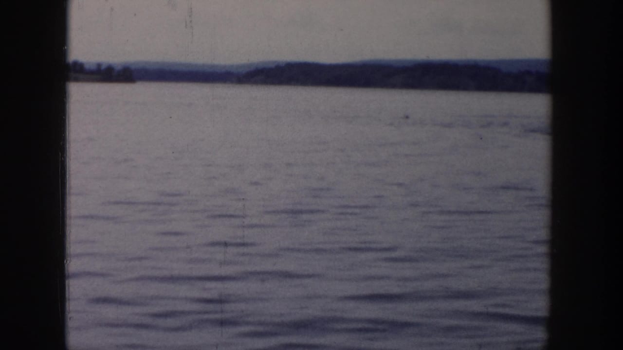 Wisconsin lake view in faded 8mm color, with calm water, a far tree line, and heavy vertical frame borders.