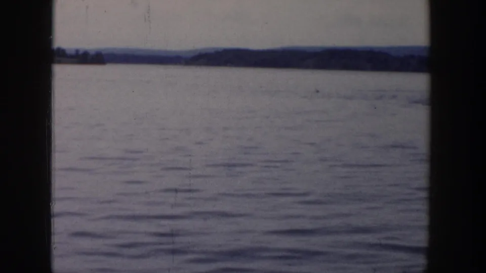 Wisconsin lake view in faded 8mm color, with calm water, a far tree line, and heavy vertical frame borders.