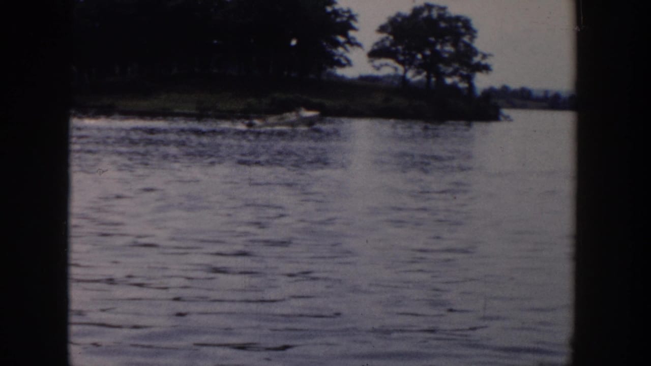 Faded 8mm view of a wooded lakeside point in Wisconsin, with rippled water, trees, and a dark home-movie frame border.