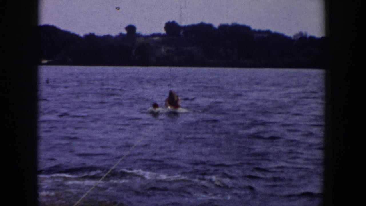 Distant water skier and another person in the lake with a tow rope leading from the camera.