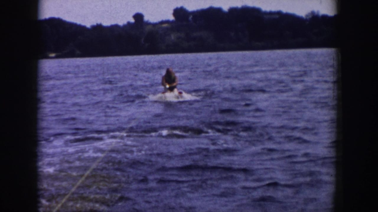Water skier being pulled across the lake, centered against a distant tree-lined shore.
