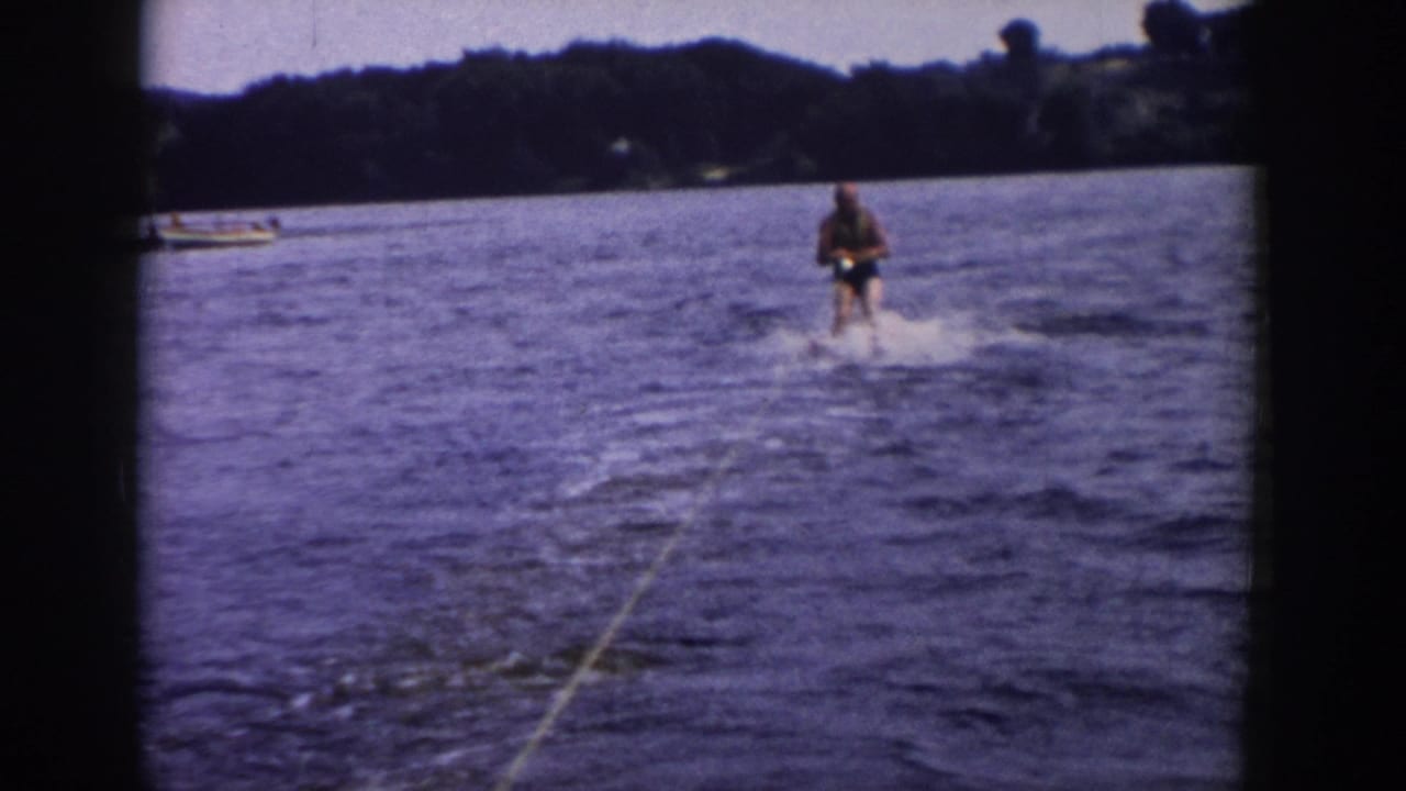 Man water skiing behind a boat on a lake with wooded shoreline in the distance.